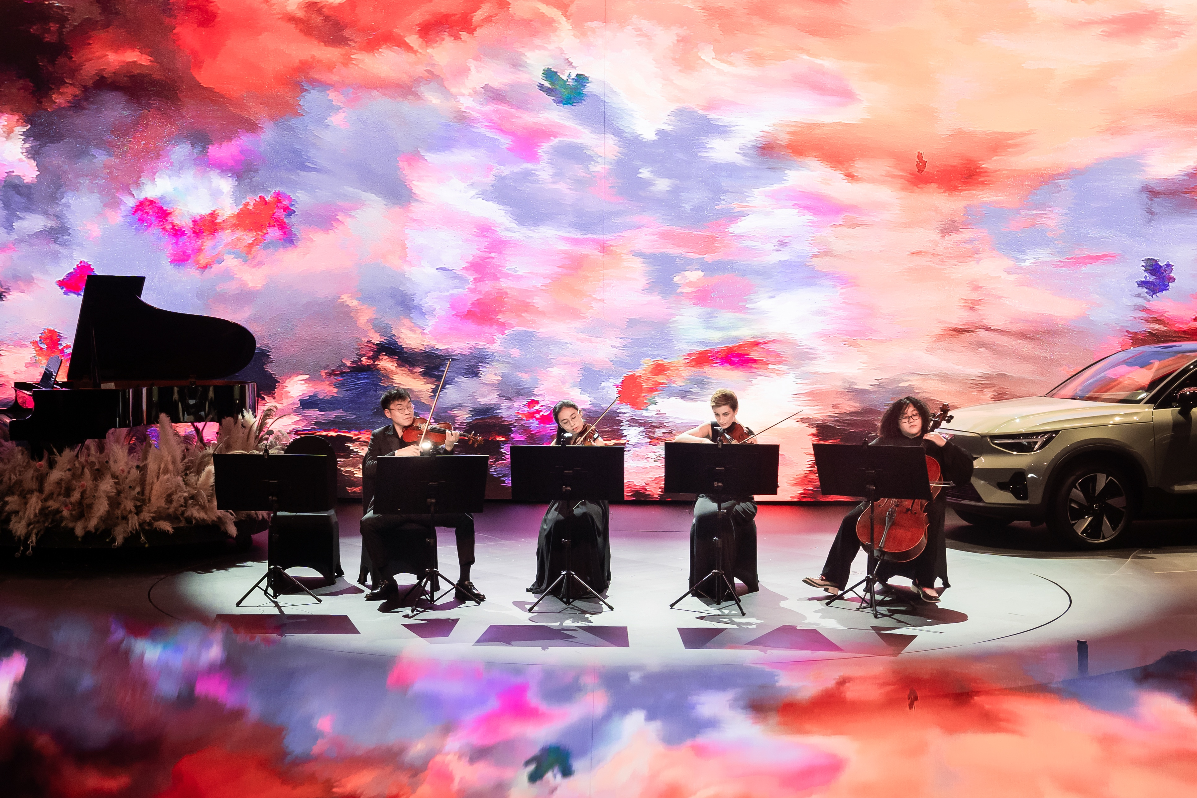 A string quartet performing on stage alongside the Volvo Car, backed by a vibrant generative sky of pinks, purples, and blues.
