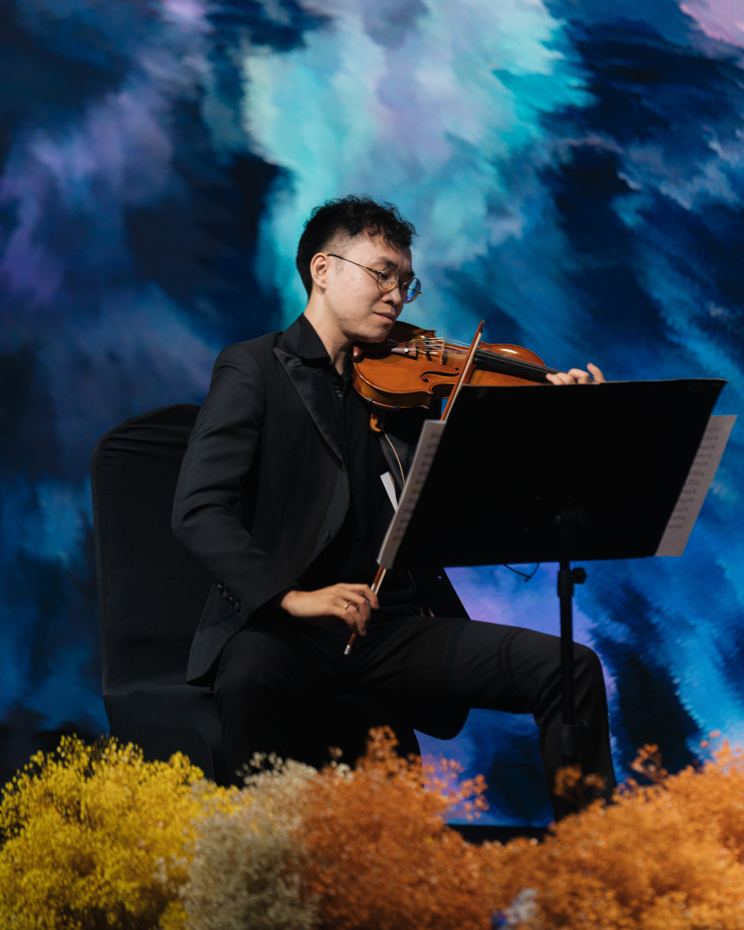 A close-up of the violinist Nguyễn Thiện Minh playing against a background of deep blues and purples.