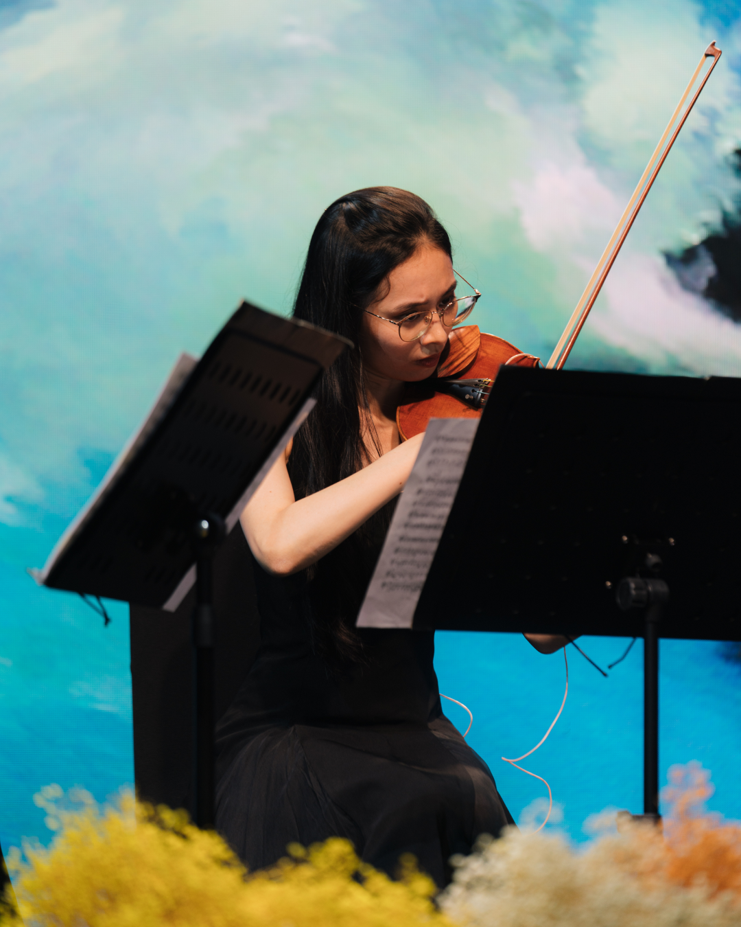 The violinist Hoàng Hồ Khánh Vân playing delicately, surrounded by ethereal blue and teal visual elements.