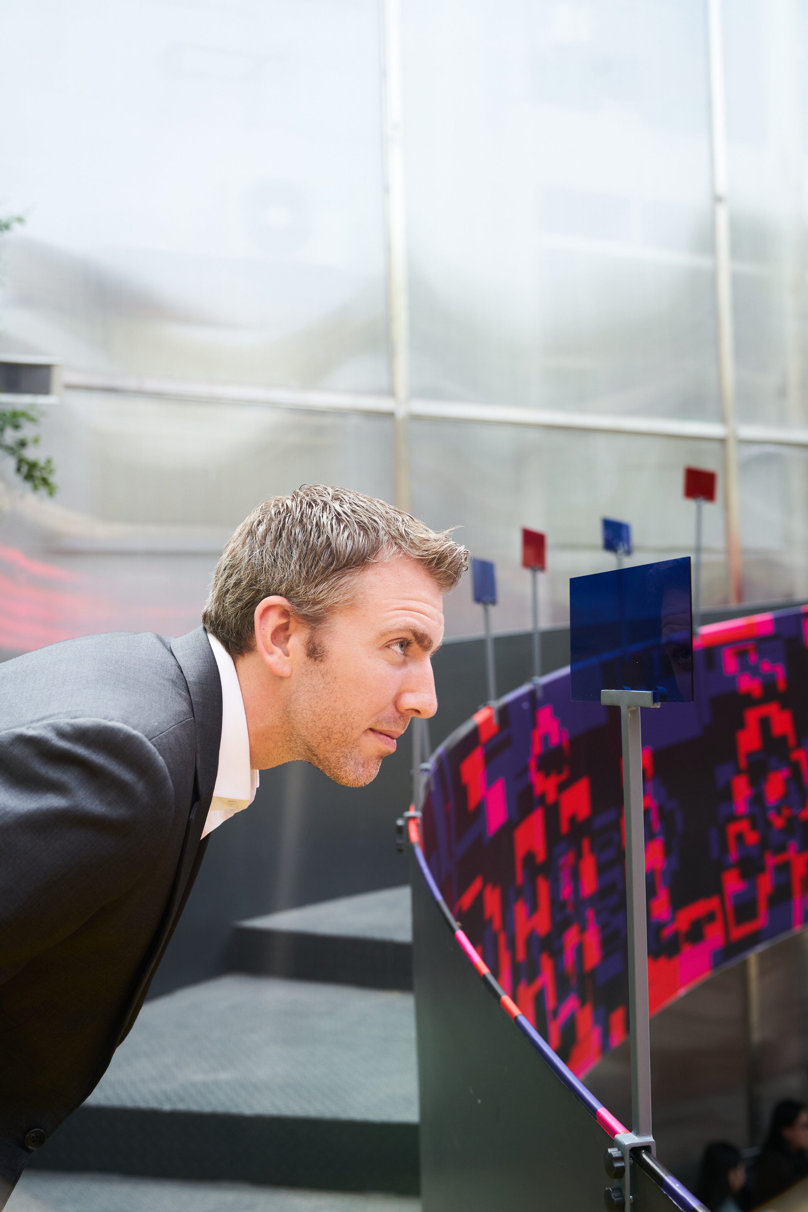 A visitor leaning in to closely examine a colorful acrylic panels sculpture at the 'Đủ' exhibition outdoor installation