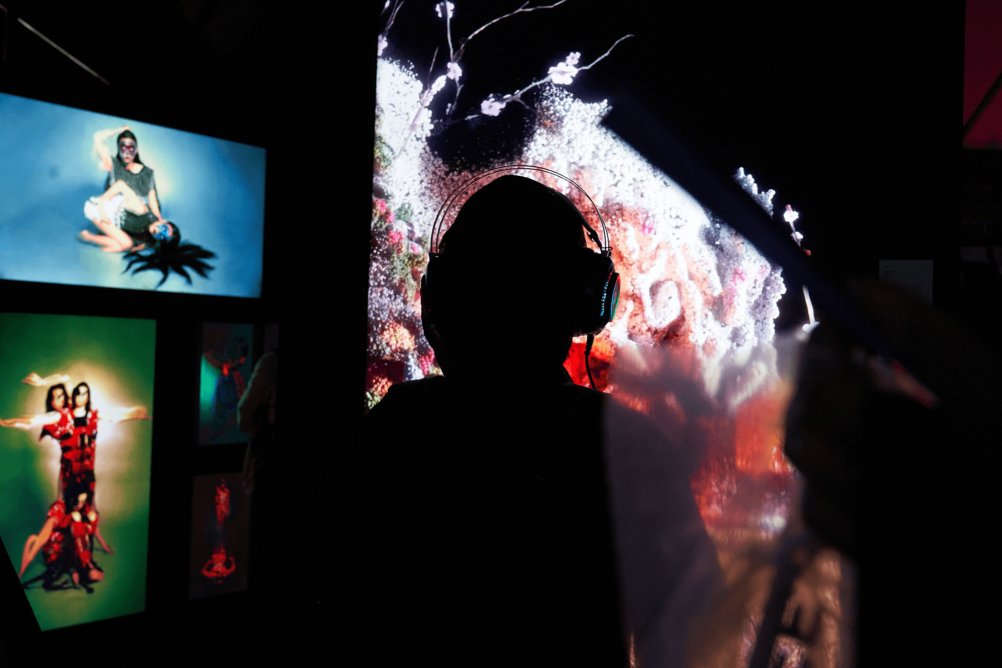 A visitor wearing headphones, watching artworks displayed across multiple screens in a darkened gallery