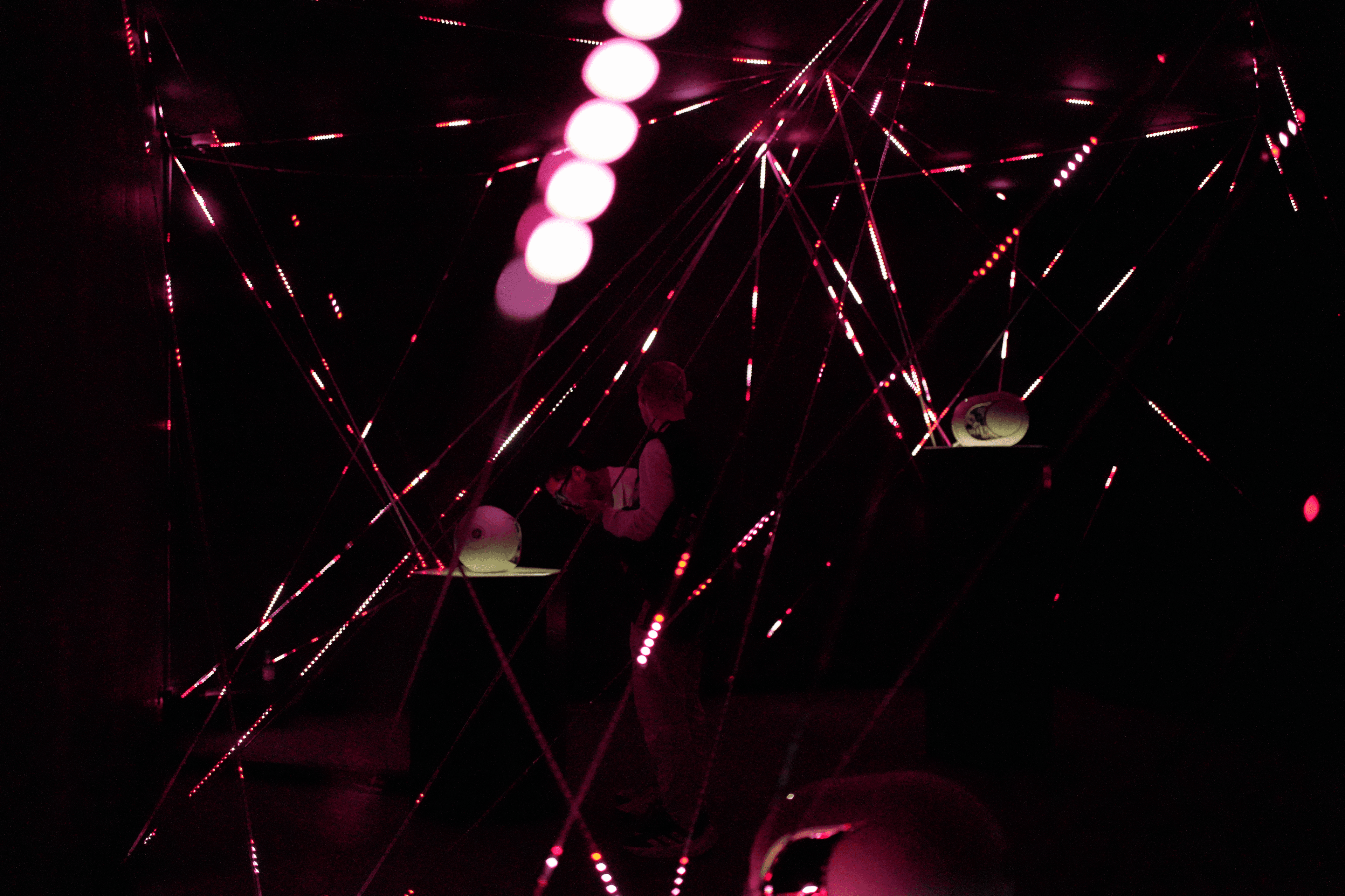 The visitors observe with a spatial sound source on a pedestal, surrounded by a web of red LED strings in the 'Silent Symphony' installation